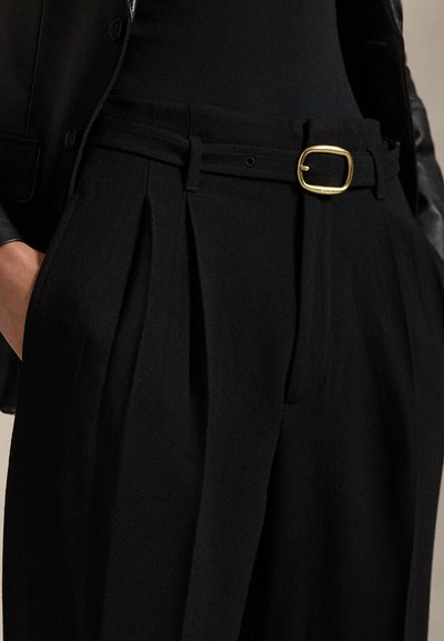 Melni piegriezti bikses ar plakstiem, gludu tekstūru un plānu jostu ar zelta taisnstūra sprādzi. Ir sānu kabatas.