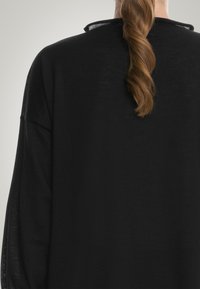 Svart, lättvikts tröja med rund halsringning och långa ärmar i en lös passform. Mjuk textur med en lätt lyster.