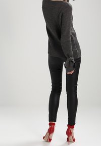 Pull gris côtelé avec un col dégagé et des poignets noués, associé à un pantalon noir ajusté et des chaussures à talons rouges.