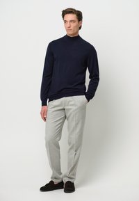 Marineblauer Rollkragenpullover, hellgraue Anzughose und dunkle Wildleder-Slipper. Die glatte Textur und die taillierte Passform schaffen einen eleganten Look.