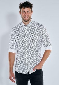 Schwarzes und weißes Hemd mit geometrischem Muster, aus leichtem Stoff gefertigt. Mit hochgekrempelten Ärmeln und Kragen.