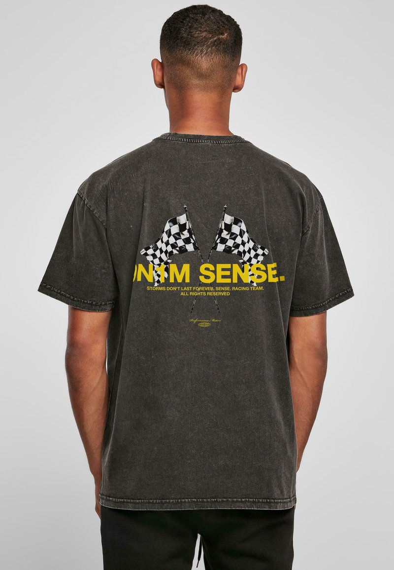 Tamsiai pilkas medvilnės marškinėliai su grafika, vaizduojančia dvi šachmatų vėliavas, ir tekstu geltona spalva. Trumpi rankovės ir laisvas kirptis.