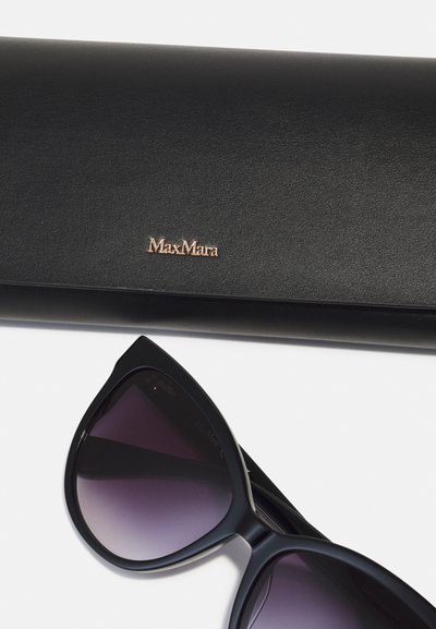 Gafas de sol negras con lentes graduales púrpuras, con una forma de ojo de gato audaz, colocadas junto a un estuche de cuero negro grabado con "MaxMara."