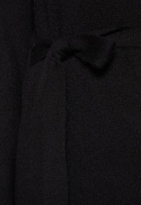 Tessuto a maglia nero con una texture morbida, caratterizzato da un accentuato nodo in vita e una finitura liscia. Vista ravvicinata dei dettagli del materiale.