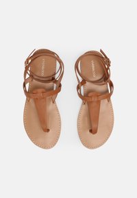 Ruske nahk sandaalit ristikkäisillä hihnoilla ja varvasosalla. Sileä pinta, vaalean värinen pohja ja ompeluyksityiskohtia reunojen ympäri.