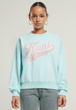 Jasnoniebieski sweatshirt z dużym, bladoróżowym logo "Kani" oraz wzorem gwiazdy, z klasycznym okrągłym dekoltem oraz ściągaczami przy mankietach i u dołu.