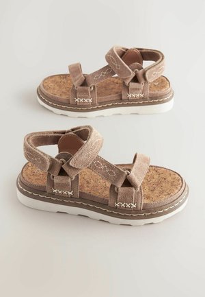 Sandales en suède marron avec semelle en liège, semelle en caoutchouc blanche et brides entrecroisées. Des accents de couture et des fermetures ajustables à la cheville.