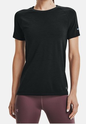 Kobieta w dopasowanej czarnej sportowej koszulce z krótkim rękawem i liliowych legginsach, stojąca z rękami swobodnie opuszczonymi wzdłuż ciała.