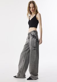 Top corto negro con tachuelas plateadas, con un dobladillo en forma de concha. Combinado con pantalones de mezclilla gris desgastado de pierna ancha y cintura alta.