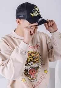 Svart keps med en gul tecknad bi-grafik, nätbak. Beige sweatshirt med en färgglad tiger-grafik och text, rund halsringning, långa ärmar.