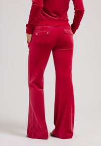 Rode velours flared broek met achterzakken en drukknoopsluitingen; zachte textuur en een aansluitende taille. Platte naden en enkellange ontwerp.