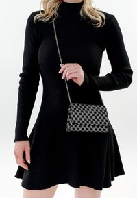 Vestido negro de manga larga acanalada con falda acampanada, combinado con un pequeño bolso cruzado a rayas en negro y gris con correa de cadena.