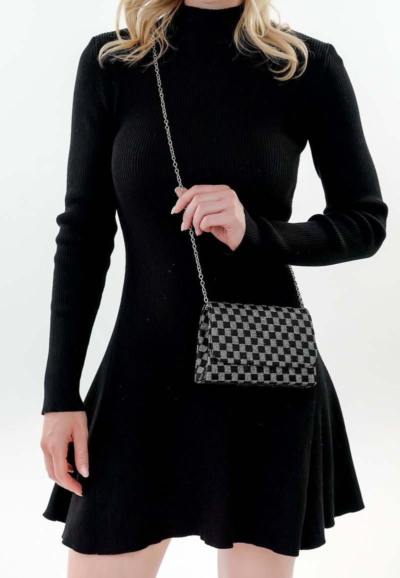 Vestido negro de manga larga acanalada con falda acampanada, combinado con un pequeño bolso cruzado a rayas en negro y gris con correa de cadena.