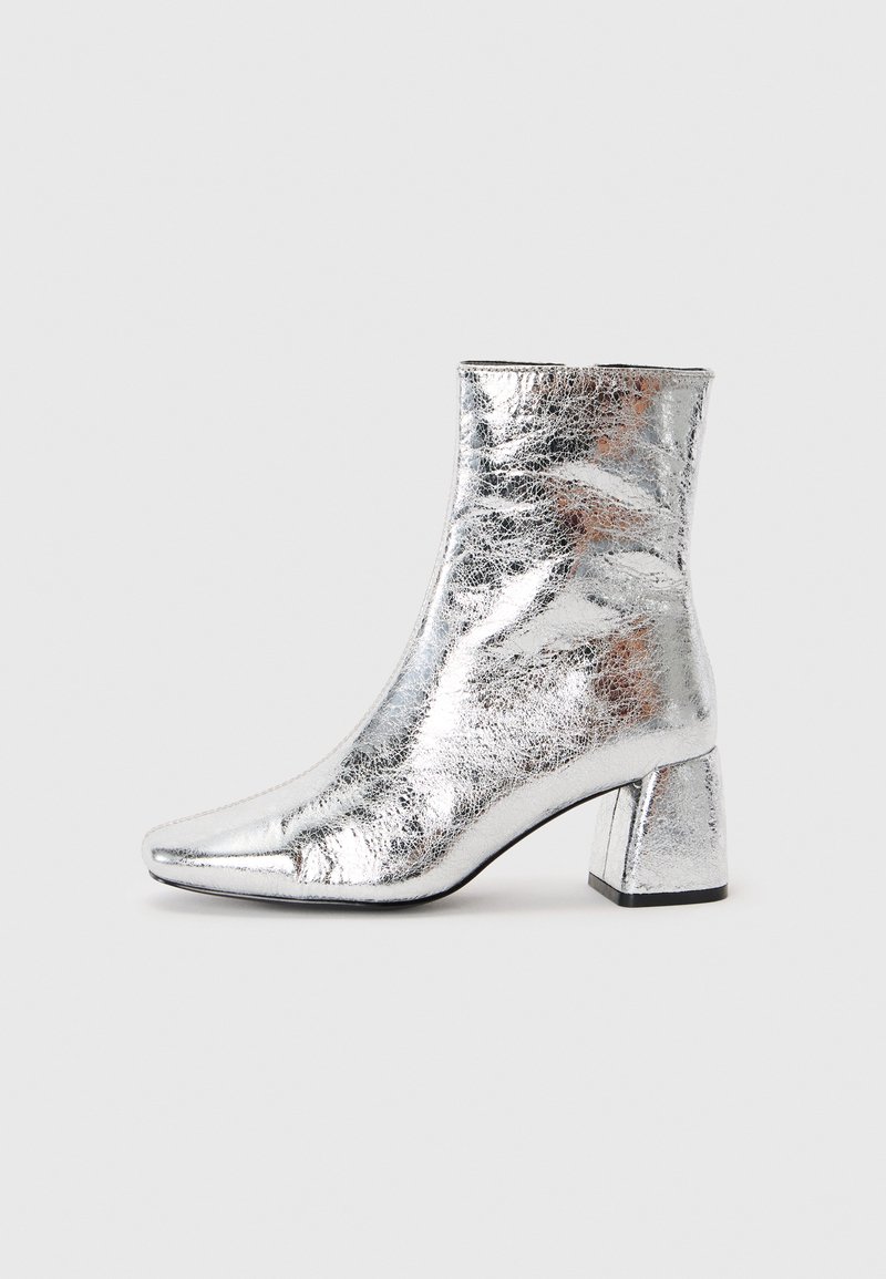 Silberne Knöchelstiefel aus glänzendem, strukturiertem Material mit einer spitzen Zehenform und einem quadratischen Absatzdesign. Reflexive Oberfläche und schlanke Form.