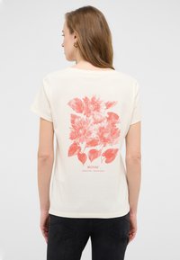 Kremines krāsas T-krekls ar lielu korallziedu printu uz muguras, kas ietver saulespuķes un lapas, ar īsām piedurknēm un brīvu piegriezumu.