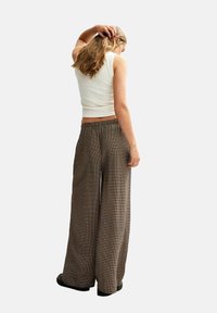 Brown and black checkered wide-leg pants with a soft texture, paired with a fitted white tank top. The pants feature an elastic waistband.