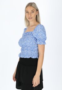 Blå blomstret top med puffærmer og firkantet udskæring samt smock-detaljer, parret med en sort lagdelt nederdel. Blødt stof og afslappet pasform.