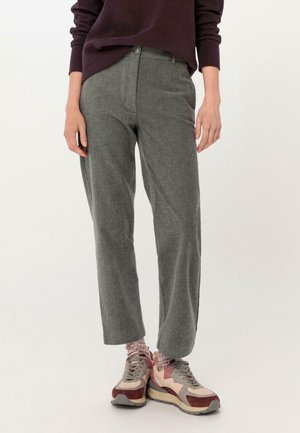 Person trägt graue, gerade geschnittene Hose, bordeauxrote und beige Turnschuhe sowie pink gemusterte Socken vor schlichtem Hintergrund.