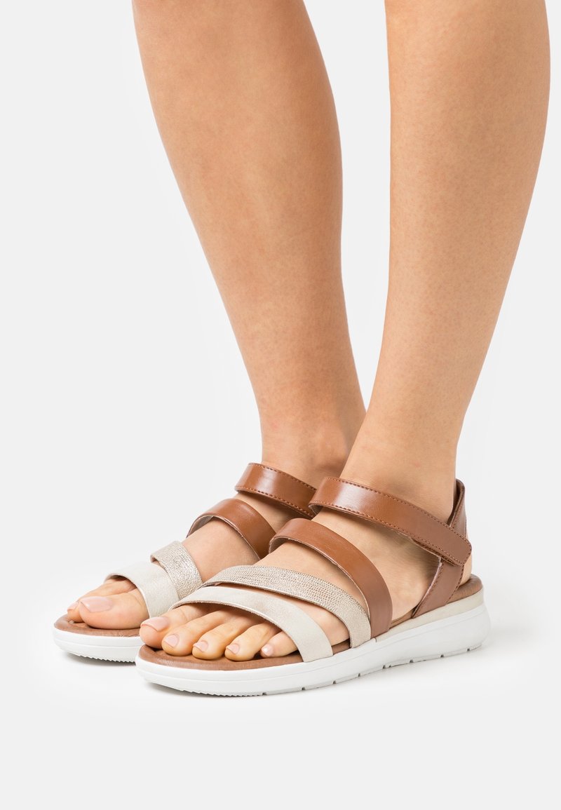 Sandales à lanières marron et beige avec un mélange de textures lisses et métalliques, dotées de deux bandes ajustables et d'une semelle blanche texturée.