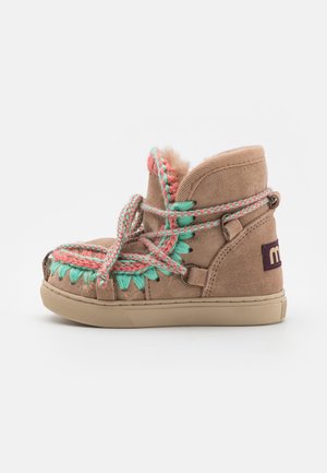 Bottines en daim beige avec des lacets tissés multicolores, doublure en peluche et coutures décoratives. La semelle est en caoutchouc beige avec un minimum d'adhérence.