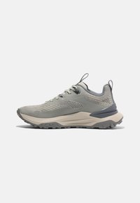 Zapatilla de trail en gris claro con parte superior de malla, detalles texturizados, puntera reforzada y suela de goma gruesa con surcos profundos para agarre.