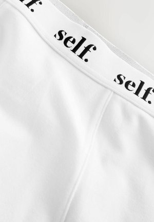 Witte stoffen tailleband met zwarte tekst "self." ontworpen in een eenvoudige, moderne lettertype; gladde textuur met zichtbare naaddetails.