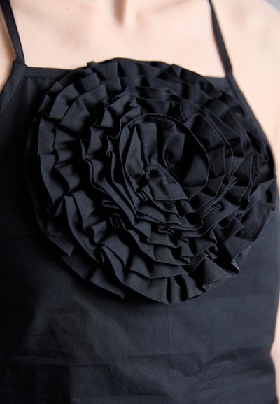 Black fabric top featuring a large, three-dimensional ruffle design resembling a flower, with varying layers and textures centrally placed.