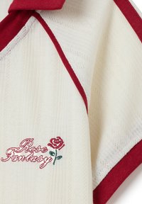 Crème brei stof met rode rand, voorzien van een geborduurde rode roos en de tekst "Rose Fantasy" in cursieve steek.