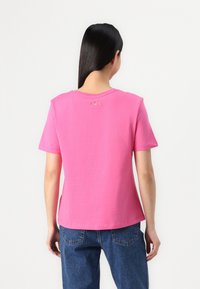 Rosa bomullströja med korta ärmar, rund halsringning och dekorativa detaljer på övre delen av ryggen. Stylad med blå denimjeans.