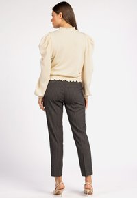 Licht beige top met pofmouwen, een rimpelrand bij de hals en onderkant, gecombineerd met donkergrijze pinstriped broek en beige hakken.