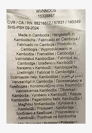 Étiquette comportant un texte multicolore sur un fond de tissu clair. Indique les détails de fabrication en plusieurs langues ; déclare principalement "Fabriqué au Cambodge."