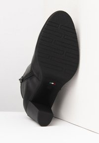 Boots en cuir noir à la cheville avec une semelle en caoutchouc texturé, un talon modeste et un détail de fermeture éclair sur le côté. Forme de orteil arrondie et plate.