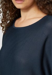 Dunkelblauer Strickpullover mit weitem Rundhalsauschnitt und strukturiertem Rippmuster. Der Stoff wirkt atmungsaktiv und hat eine weiche Textur.