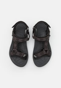 Zwarte sandalen met gestructureerde stoffen banden met een bruin geometrisch patroon, verstelbare sluitingen en een rubberen zool met patroon.