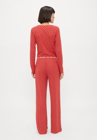 Roter Pyjama-Set mit Punkten, bestehend aus langärmligem Oberteil und weit geschnittenen Hosen. Der Stoff ist weich mit einer dezenten Textur und einem dekorativen Taillenbund.