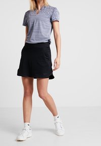 Šedý pruhovaný polo triko s krátkým rukávem, v kombinaci s černou A-liniovou sukní. Bílé tenisky a kotníkové ponožky dotvářejí sportovní vzhled.