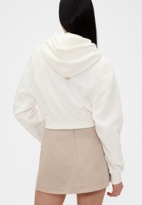 Avkortet hvit hettegenser med stor hette, mykt stoff og ribbet kant; kombinert med en beige miniskjørt. Jevn tekstur.