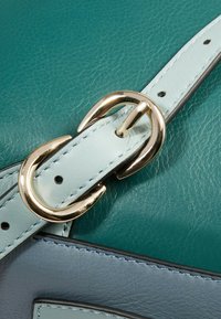 Correa de bolso de cuero verde azulado con detalles en azul pálido, con hebilla metálica dorada y detalles de costura. Textura suave con acabado pulido.