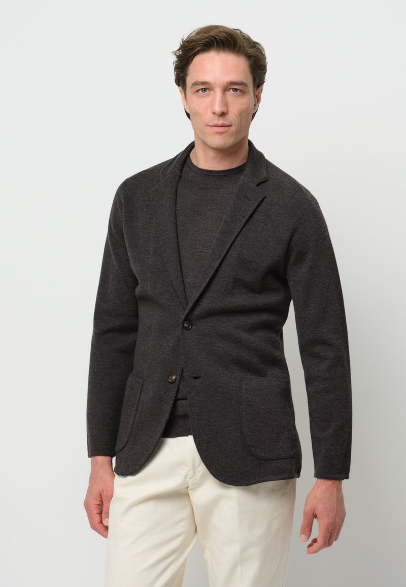 Dunkelgrauer Blazer mit spitzem Revers, einem Knopf und zwei Vordertaschen. Trägt man über einem dunklen Pullover und kombiniert mit beigen Hosen.