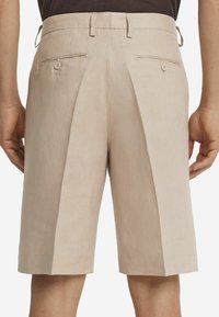 Beige Leinen-Shorts mit gefaltetem Vorderteil, elastischem Bund an der Seite und zwei hinteren Taschen mit Knopfverschluss. Flacher Saum.