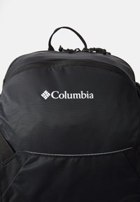 Svart stoffryggsekk med glidelåslomme, som har "Columbia"-logoen i hvitt. Glatt tekstur og robuste stropper.