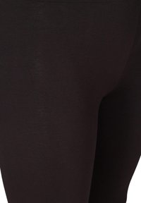 Leggings noirs en matériau extensible, avec une texture lisse et une taille haute pour un ajustement confortable. Gros plan sur le détail du tissu.