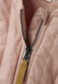 Tissu matelassé rose clair avec une fermeture éclair noire et une tirette jaune. Le tissu a une texture lisse et une couture visible le long des coutures.