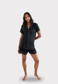 Czarny zestaw piżamowy składający się z bluzki z krótkim rękawem, kołnierzykiem i kieszonką, w komplecie z dopasowanymi szortami, wykończony białymi lamówkami.
