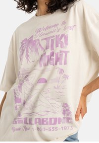 Kremowa, oversize koszulka z różowym nadrukiem przedstawiającym tropikalny krajobraz, kobietę oraz tekst „Tiki Night” od Billabong.