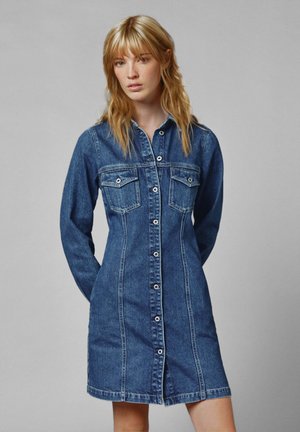 Robe chemise en denim bleu foncé. Elle possède des manches longues, deux poches poitrine, une fermeture à boutons et des coutures visibles pour plus de texture.