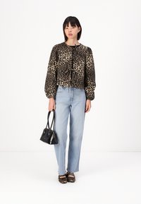 Blůza s leopardím potiskem a balónovými rukávy, kombinovaná se světle modrými džíny rovného střihu a černou mini kabelkou. Modelka má na sobě černé sandály na pásky.