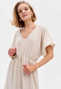 Beige, knielange jurk met V-hals, korte batwing-mouwen. Trekkoord in de taille, met een textuurafwerking langs de mouwen. Soepele stof.