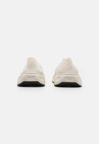 Baskets de sport beige clair avec une tige en mesh texturé, un col rembourré et une semelle en caoutchouc noir. Présente un design élégant et minimaliste.