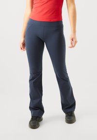 Marineblaue ausgestellte Hose aus elastischem Material. Hat eine glatte Textur und Flachnähte, kombiniert mit einem figurbetonten roten Oberteil und schwarzen Schuhen.